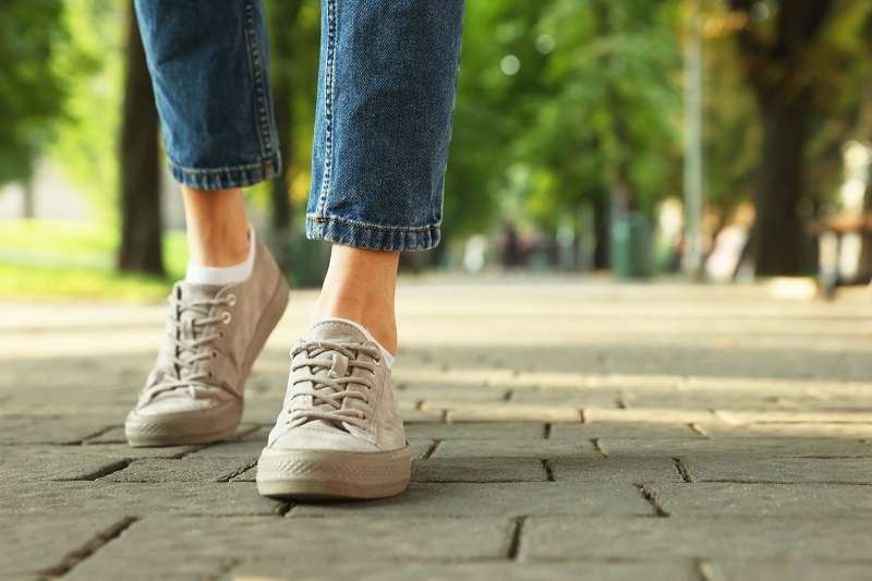 Close-up of feet in sneakers walking on a sidewalk, motion showing daily steps