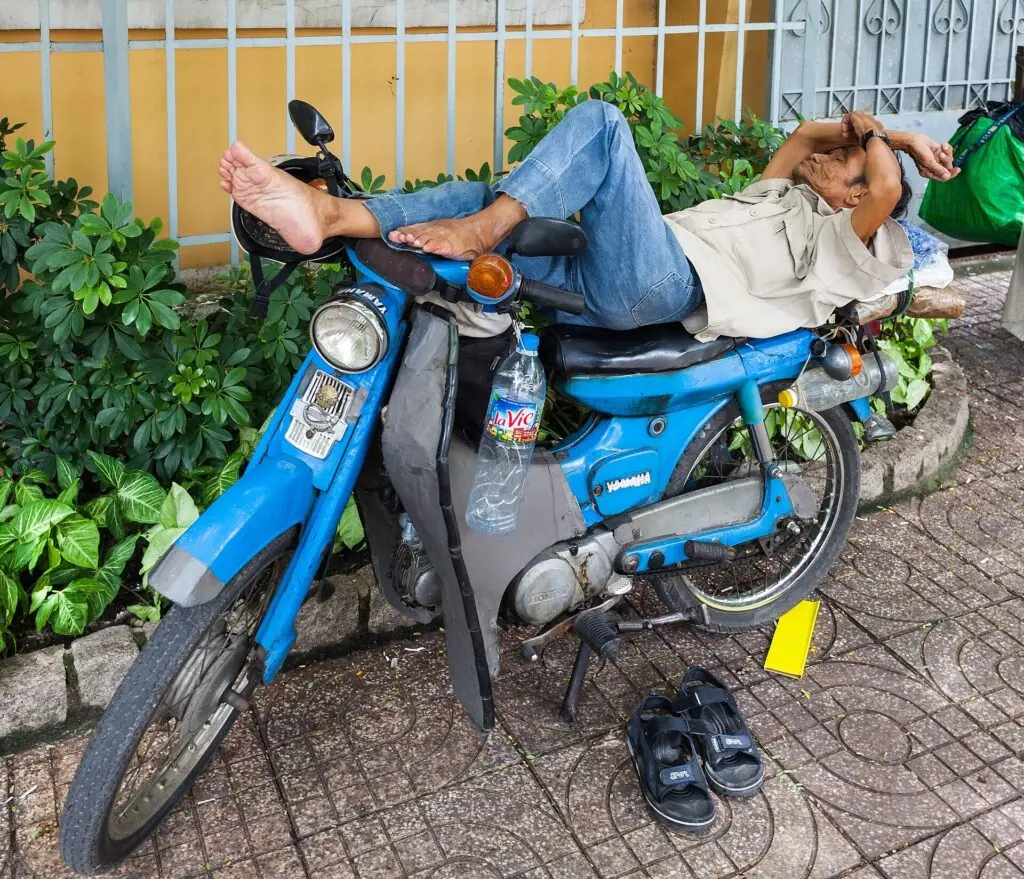 Man taking an afternoon nap stretched across a parked motorbike in Ho Chi Minh City