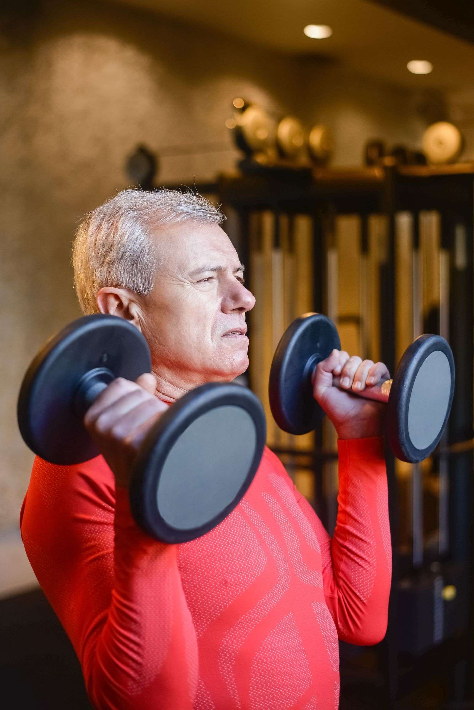 Older man doing a dumbbell shoulder press in a gym, one of the best exercises for bone density