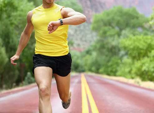 A runner checks the fitness watch on his wrist while training outdoors on a paved road.