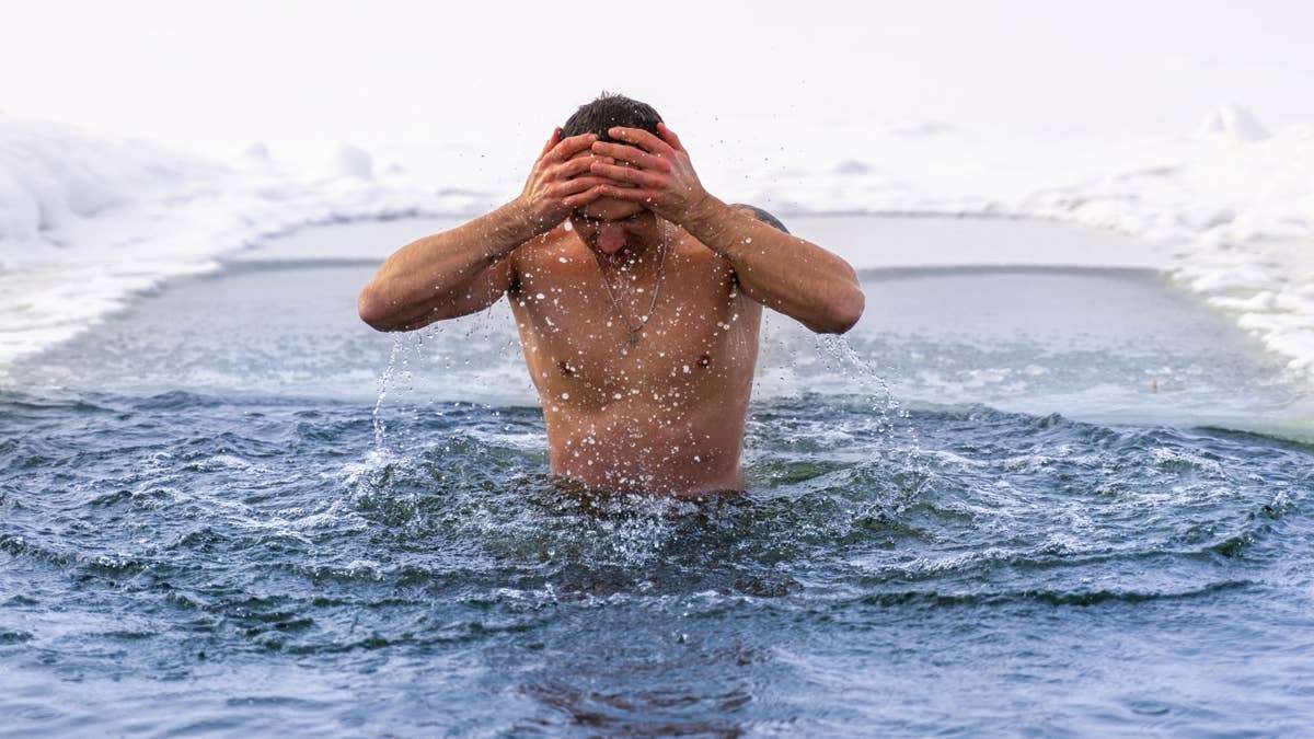 A man takes an ice bath in freezing open water, splashing cold water over his head.