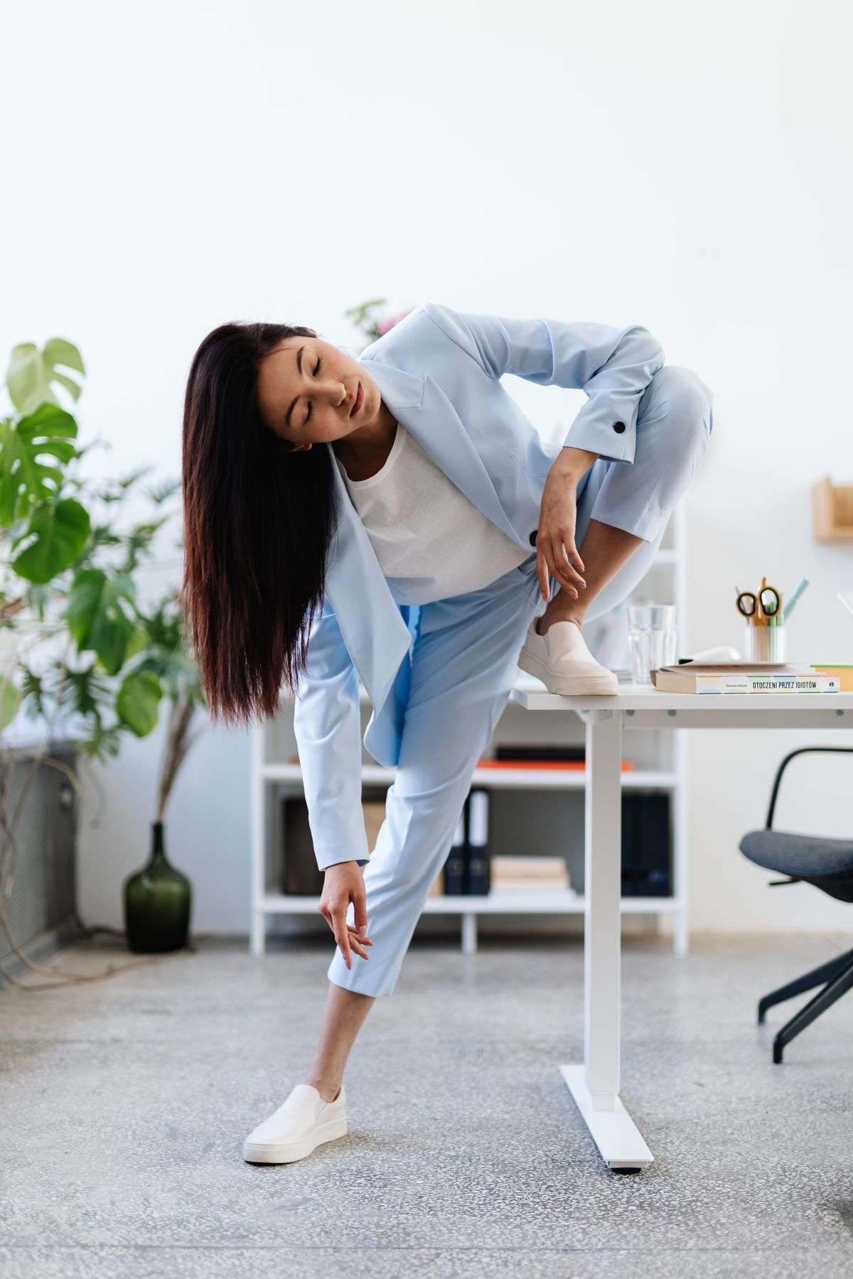Woman doing a standing stretch beside her office desk, one of the exercises for people who sit all day