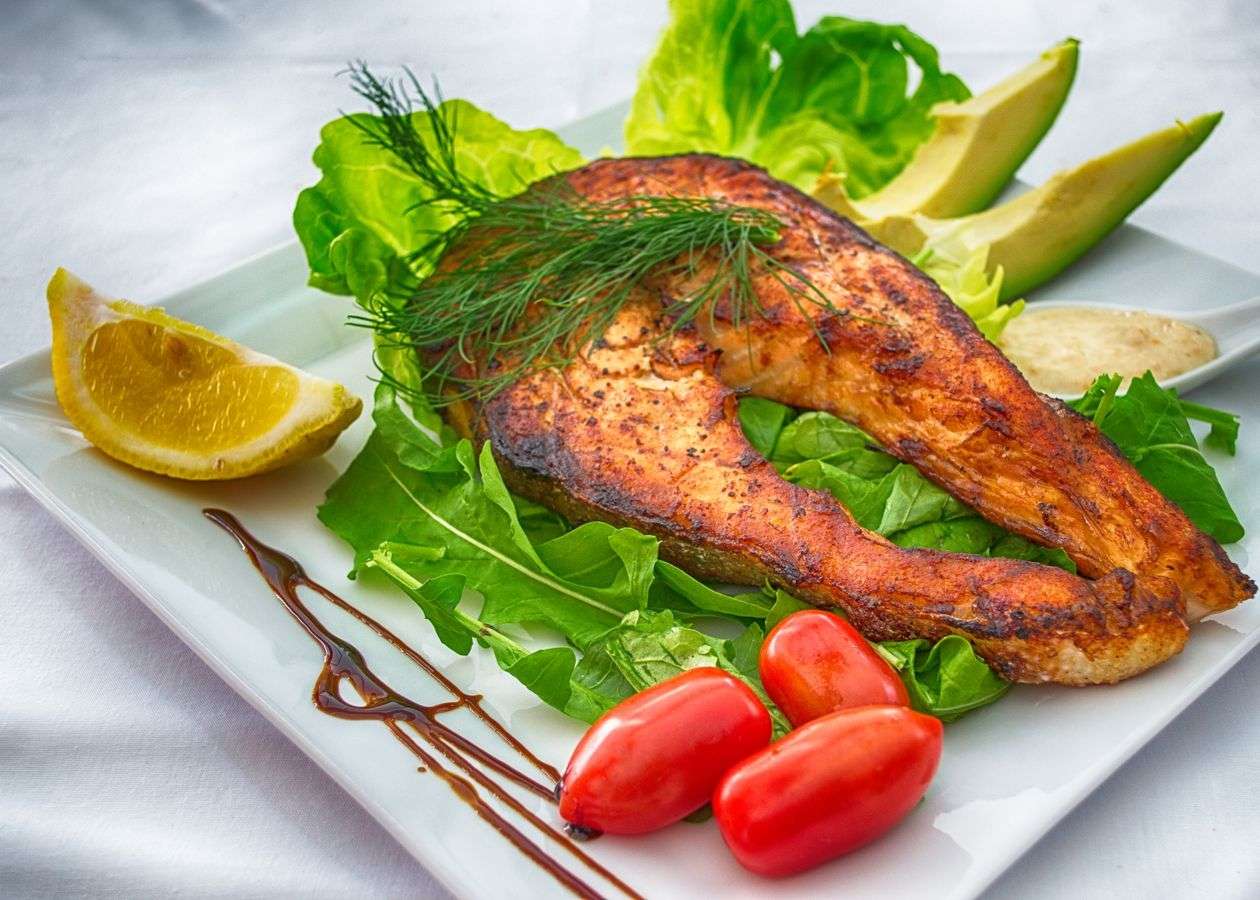 Grilled salmon with avocado and lemon on a plate, two of the most evidence-backed foods that lower cholesterol fast.