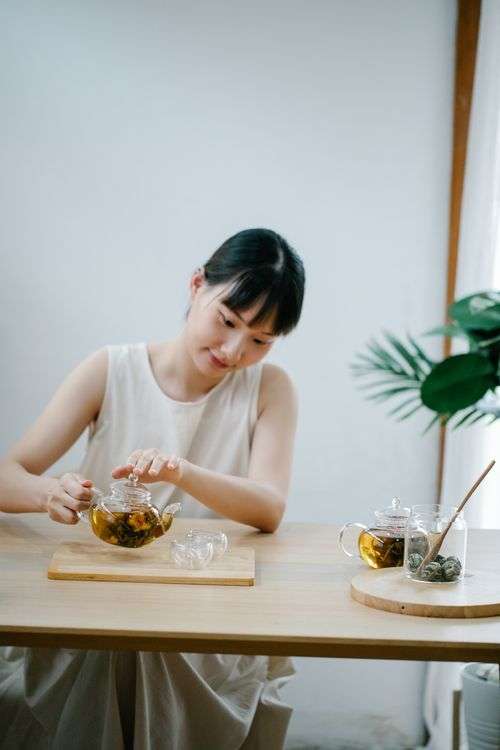 Woman pouring herbal tea at a wooden table, a calm morning ritual for women practicing intermittent fasting