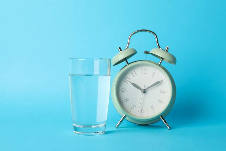 Close-up of a clock next to a glass of water, symbolizing time-restricted eating windows