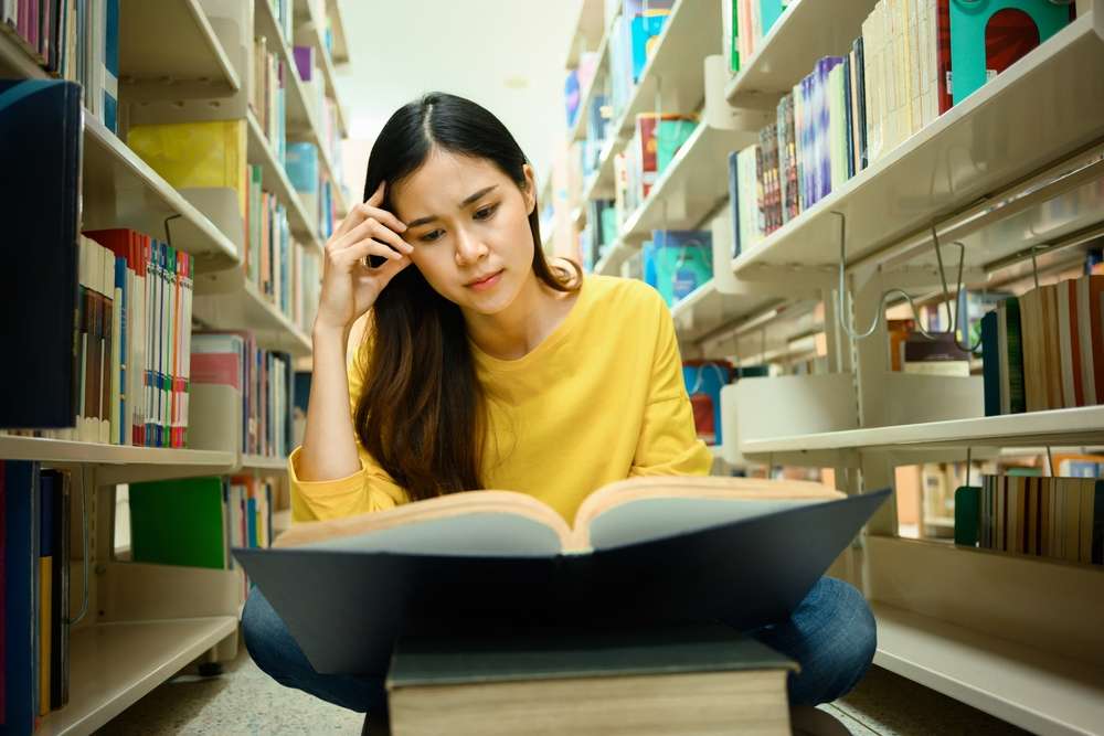 Person studying with focus at a desk surrounded by books in a library