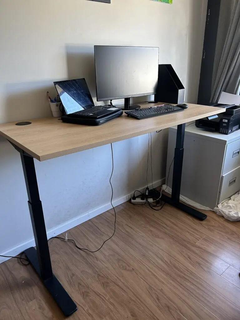 Height-adjustable standing workstation with monitor, laptop, and keyboard in a home office